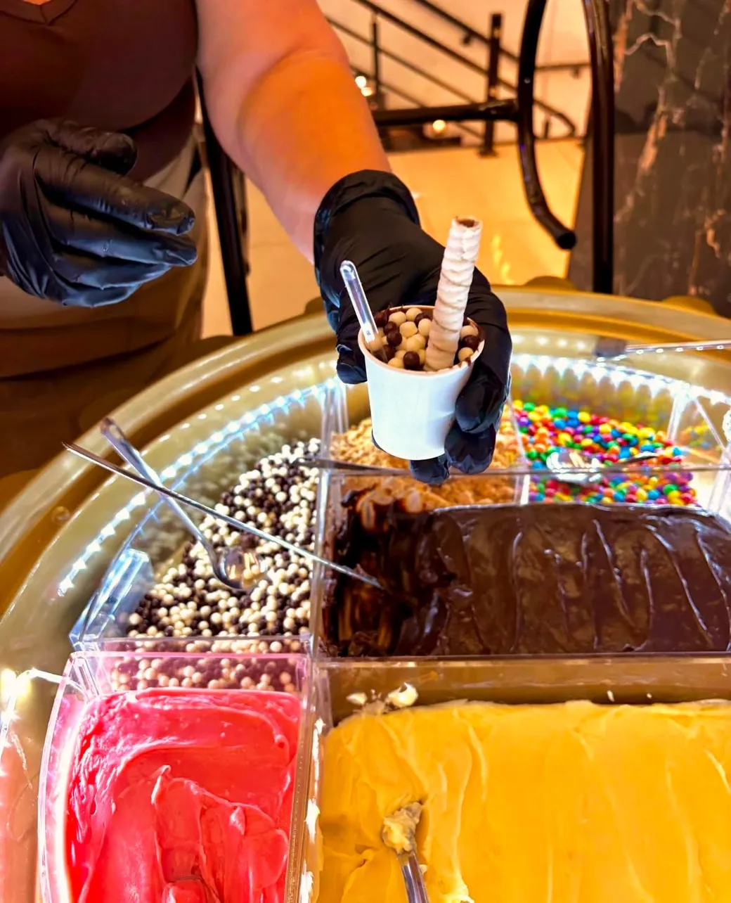 Promotora do Brigadú de luva preta entregando um copinho de brigadeiro com chocoball e canudo de wafer
