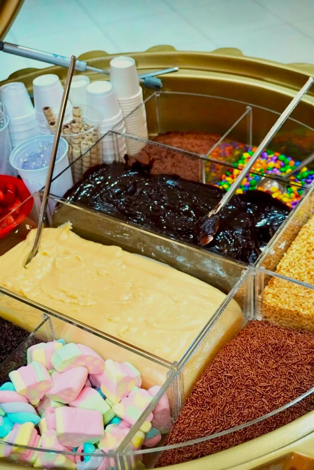 Close das cubas do carrinho Brigadú com marshmallow, granulado de chocolate, brigadeiro branco, ganache e confetes coloridos